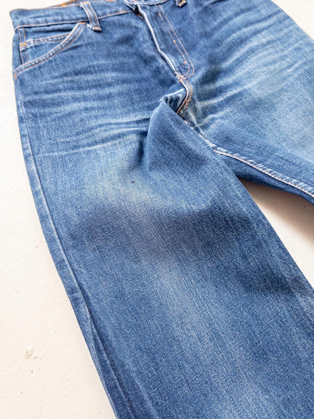 Nahaufnahme der Vorderseite der Levis W25 mit Fading-Spuren und typischer 70s Waschung.. Die Jeans hat ein klassisches Fünf-Taschen-Design mit sichtbaren Abnutzungserscheinungen und Ausbleichen. Der Stoff hat ein strukturiertes Aussehen und die Nähte sind in einer Kontrastfarbe gehalten.