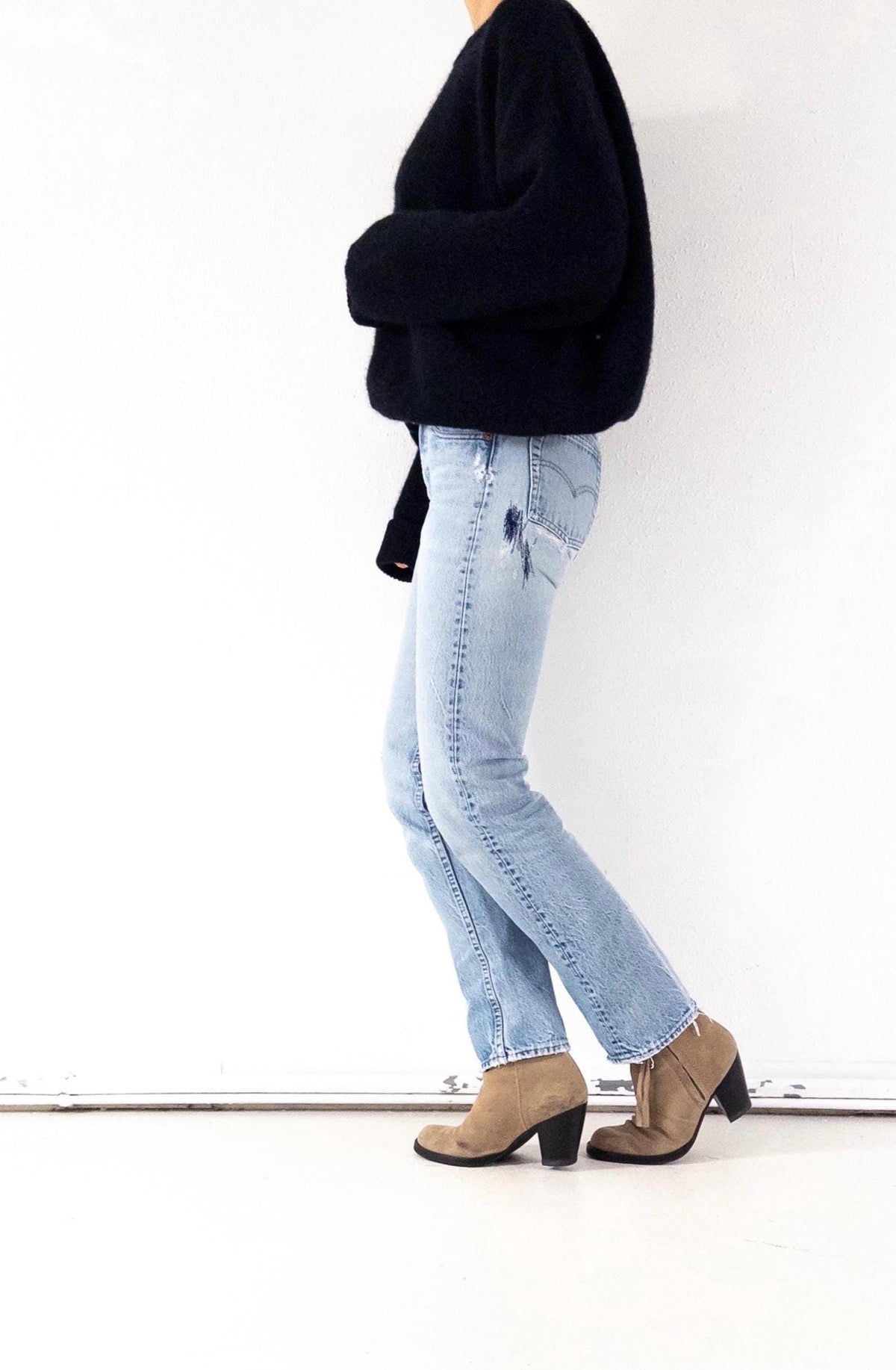 Könnte beinhalten: Eine Person trägt einen schwarzen Pullover, hellblaue Jeans mit Distressed-Details und hellbraune Wildleder-Ankle Boots mit schwarzen Absätzen. Das Outfit ist lässig und stilvoll, geeignet für den Alltag.