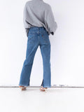 Könnte beinhalten: Eine Person trägt einen grauen Pullover und eine blaue Jeans. Die Jeans hat einen Schlitz am Knöchel und ein rotes Levi's-Etikett auf der Gesäßtasche. Die Person trägt weiße Absätze.