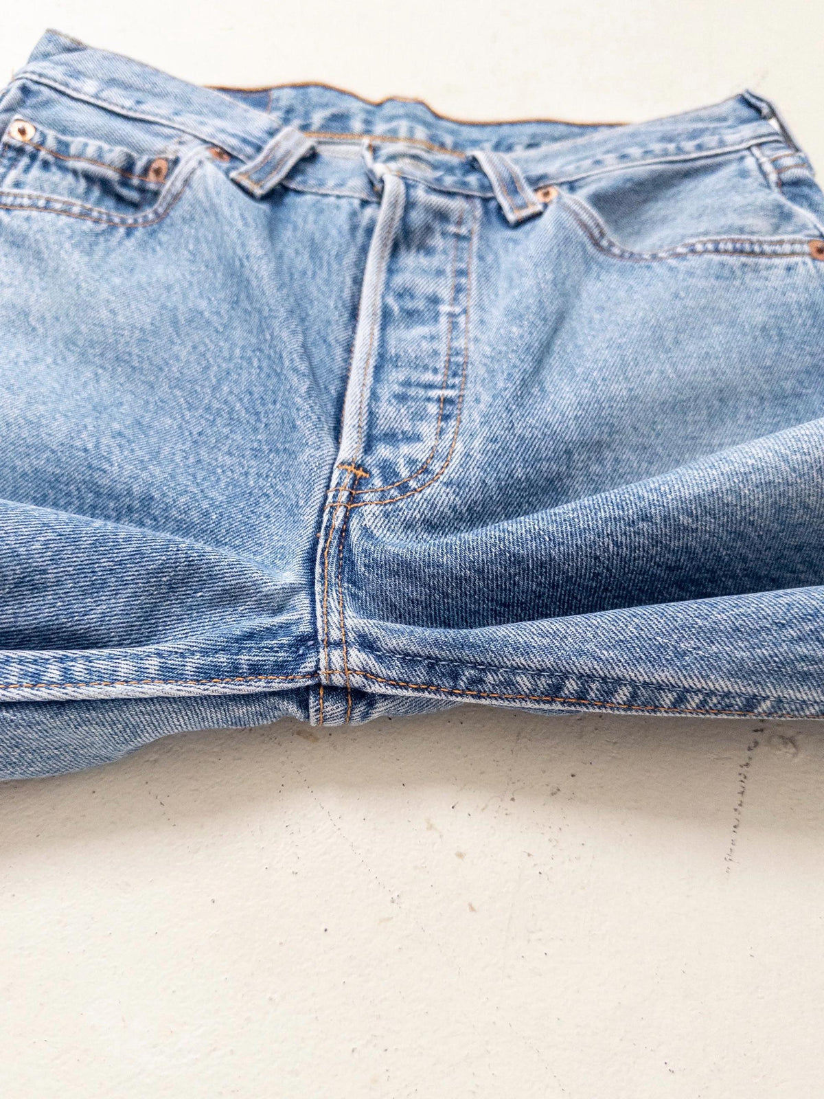 Detailaufnahme der hellblauen Levis 501 Vintage Jeans flach liegend. Zeigt Bund, Gürtelschlaufen und die typische Button-Fly-Knopfleiste im Nahbereich.
