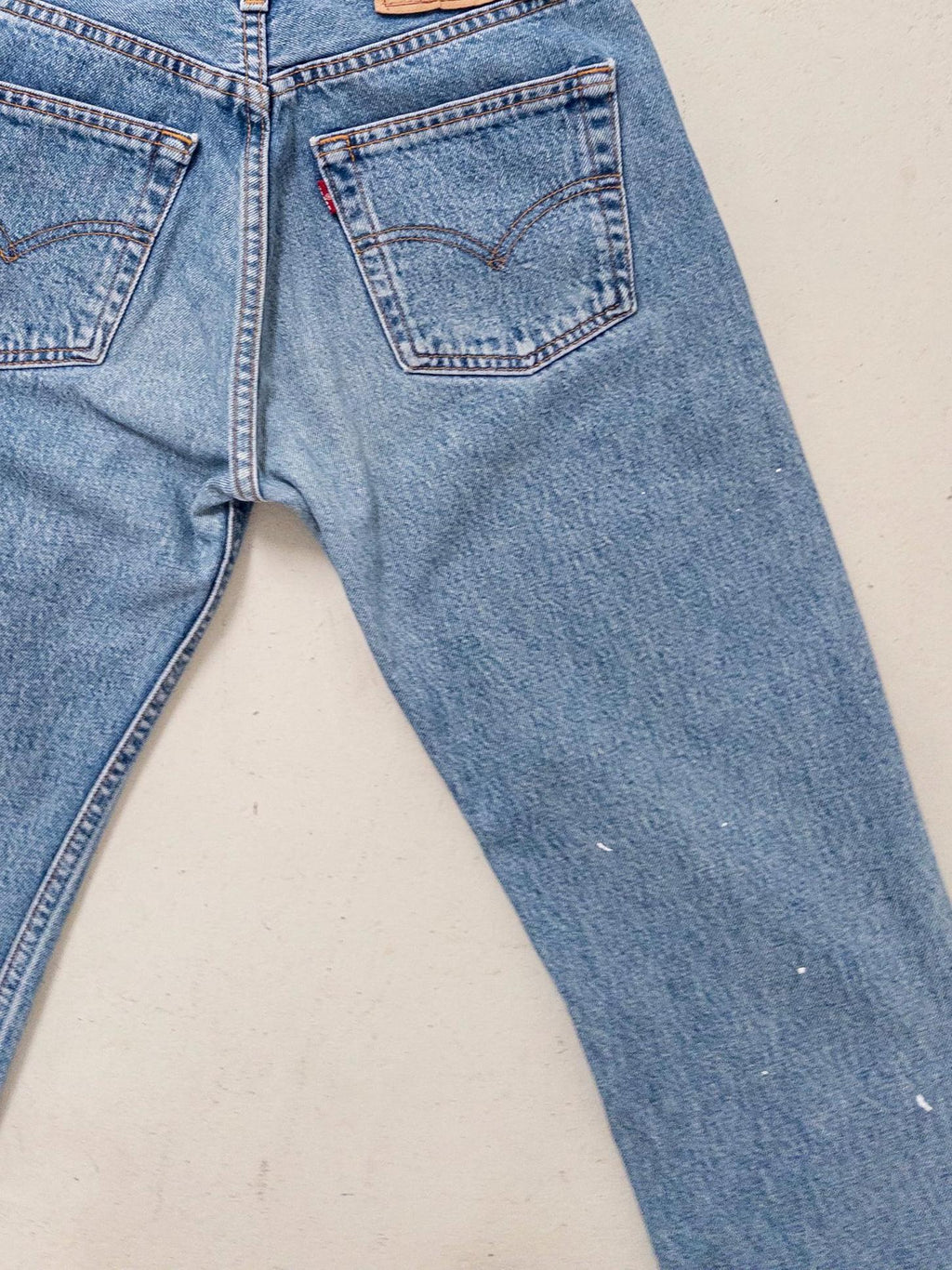 Nahaufnahme der Rückseite der hellblauen Levis 501 flach ausgelegt mit Fokus auf den Lederpatch am Bund und die symmetrischen Gesäßtaschen. Auf dem rechten Bein sieht man die zarten, weißen Farbkleckse, die diese Jeans one of a kind machen.