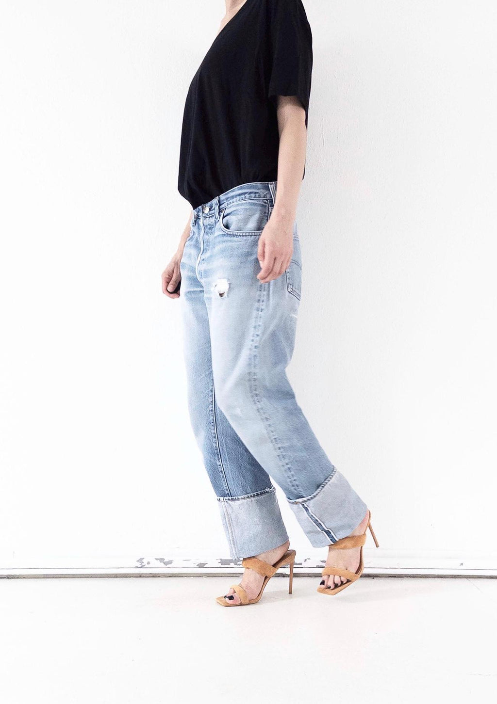 3/4-Frontansicht der hellblauen Vintage Levi’s 501 Selvedge Jeans im soft worn Grunge Distressed-Look mit doppeltem Umschlag. One of a kind Unikat gestylt mit schwarzem V-Top und filigranen Heels. Thrashed Vintage Denim von girlstalkvintage.