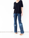 Frontansicht der Vintage 70s Lee Flared Jeans W23 W24 mit angewinkeltem Bein. Sun Faded Darkwash Schlaghose, gestylt mit schwarzem T-Shirt mit V-Ausschnitt und Highheels aus braunem Wildleder.