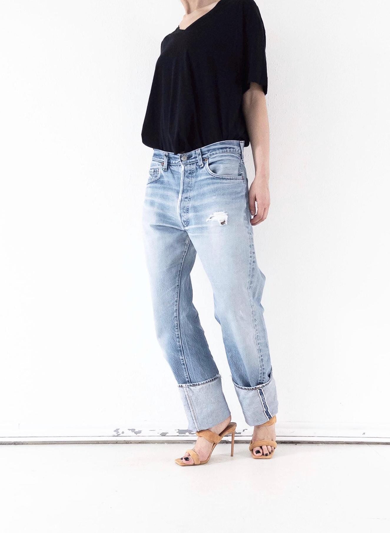 Frontansicht der  Levi’s 501 Selvedge mit authentischer Waschung in Hellblau (Light Wash), leichtem Distressed-Look am Oberschenkel und gekrempeltem Saum.
girlstalkvintage stylt dazu ein locker fallendes schwarzes V-Neck-Top mit halblangen Ärmeln, das  in den Bund gesteckt ist (French Tuck), um eine feminine Silhouette zu betonen.
Dazu elegante, minimalistische Highheels , die dem thrashed Denim-Look eine feminine Note verleihen und die Beine optisch verlängern.