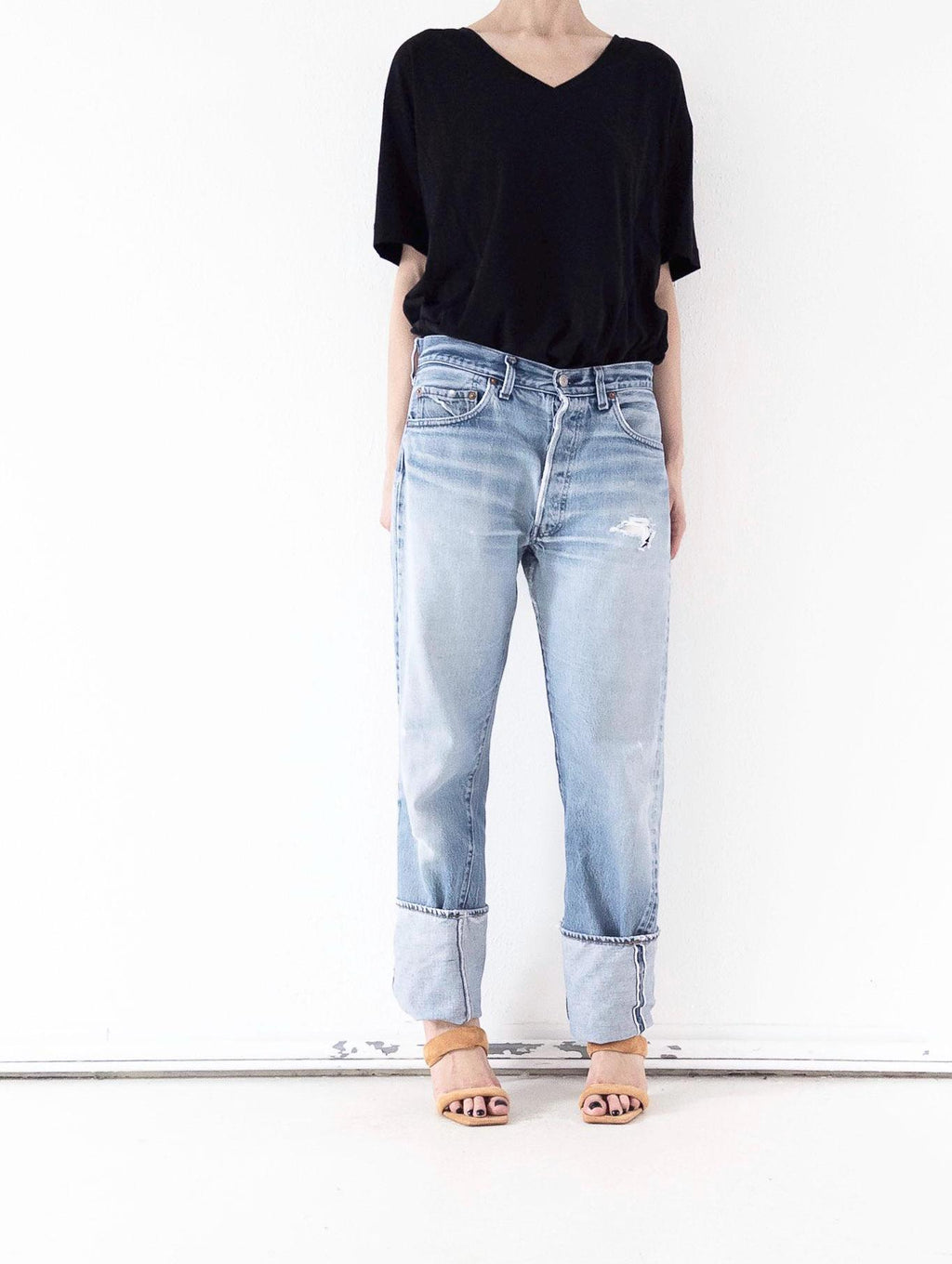 Hellblaue Levi’s 501 Selvedge Jeans in der Frontansicht. Vintage One of a Kind Unikat mit dezenter Grunge-Waschung, Distressed-Details am Oberschenkel und Umschlag. Gestylt mit lockerem schwarzem V-Shirt und Sandaletten von girlstalkvintage.