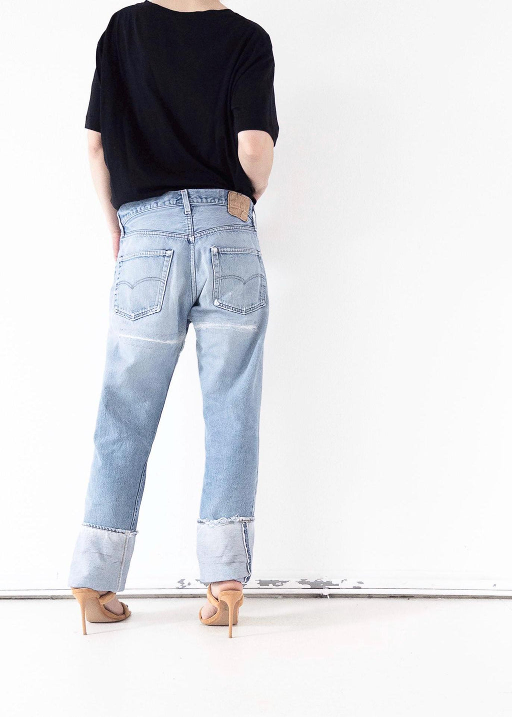 Rückansicht der hellblauen Vintage Levi’s 501 Selvedge Jeans im Grunge Distressed-Look mit breitem Umschlag. One of a kind Styling mit schwarzem Top und filigranen High Heels. Authentischer 80s Thrashed Denim von girlstalkvintage.