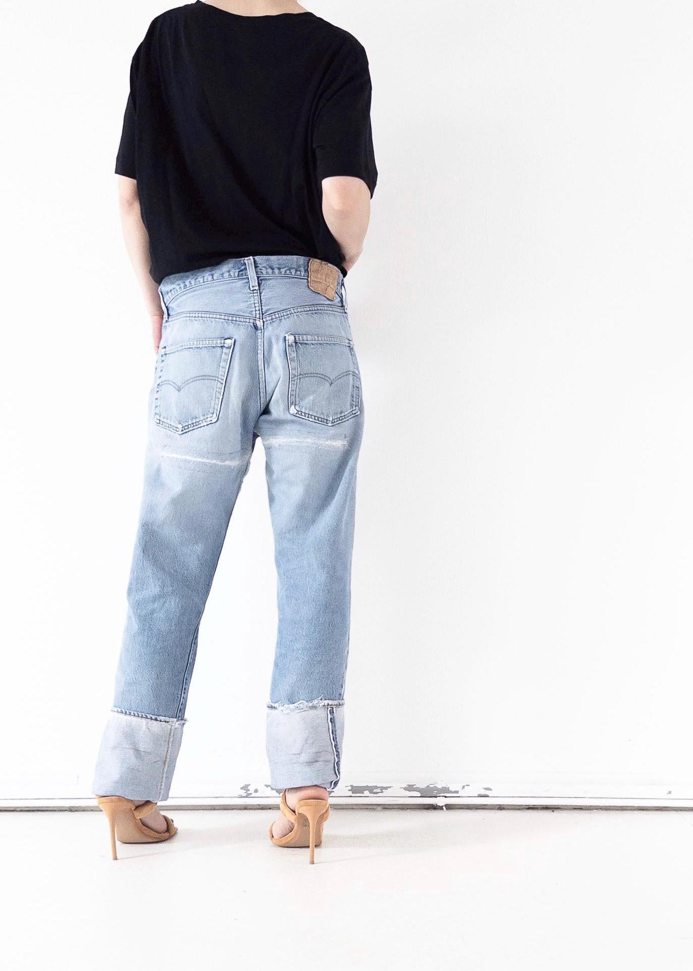 Rückansicht der hellblauen Vintage Levi’s 501 Selvedge Jeans im Grunge Distressed-Look mit breitem Umschlag. One of a kind Styling mit schwarzem Top und filigranen High Heels. Authentischer 80s Thrashed Denim von girlstalkvintage.