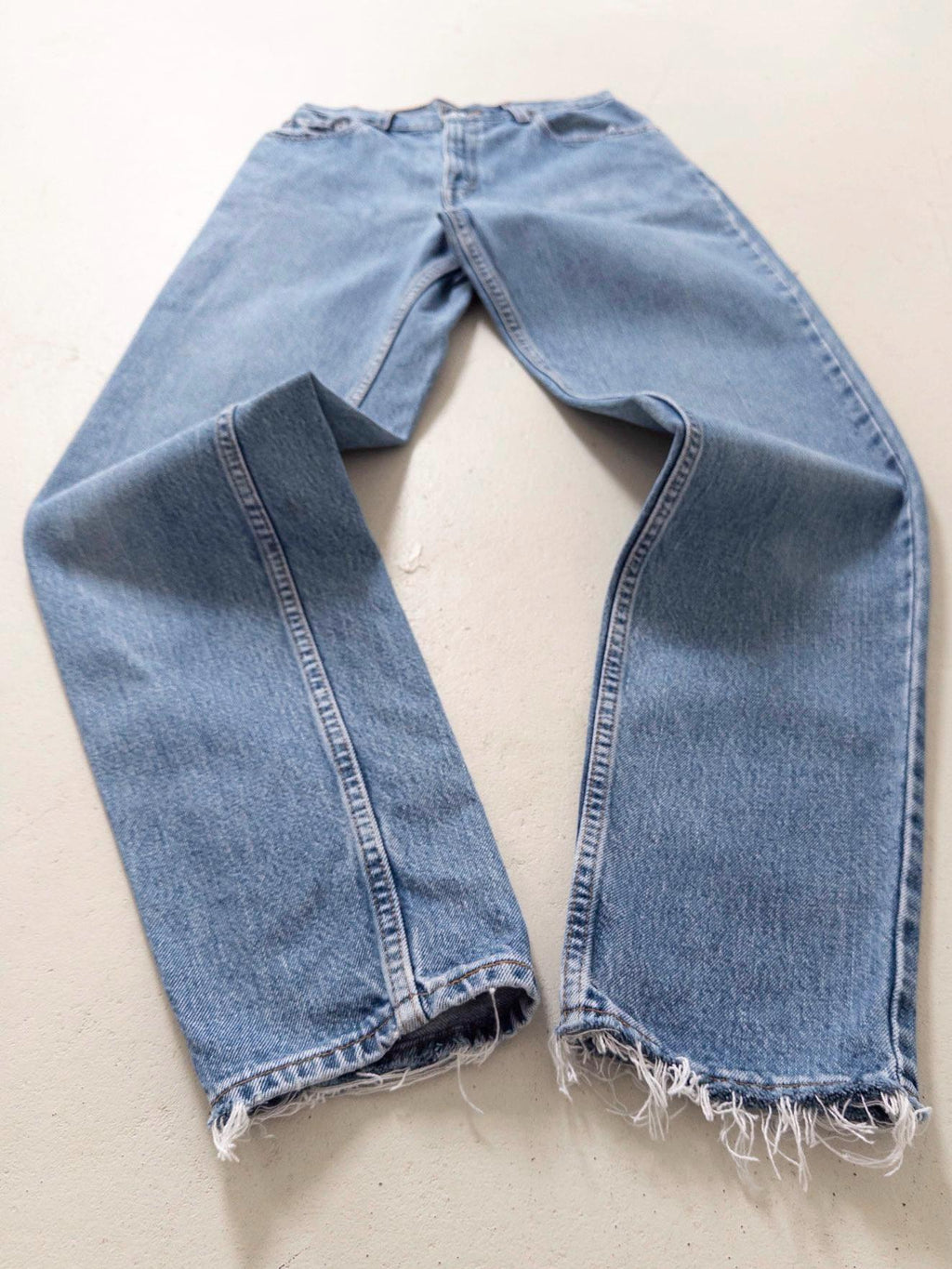 Flatlay Vorderansicht Vintage Levis 550 High Waist Jeans W26 L34 mit Fokus auf den Saum. Liegendes Produktfoto mit Details wie ausgefransten Taschen & Saum